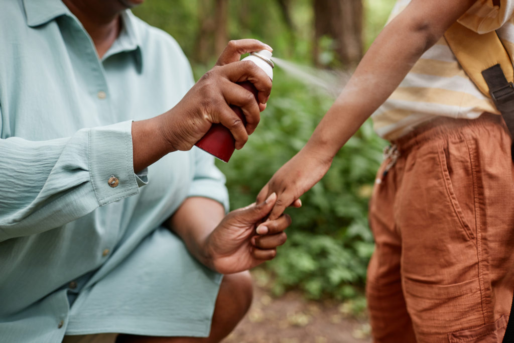 Closeup of caring black mother using baby safe bug repellent for da